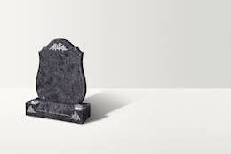 A dark blue-grey granite heandstone with an arc top. There are thistle ornaments on the top and two at the base, underneath two vases.