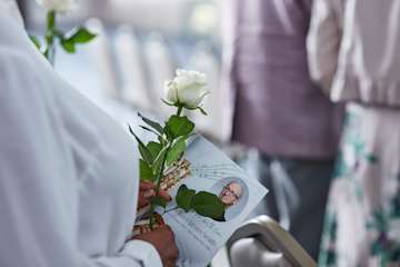 Woman holding a rose and an order of service at a funeral