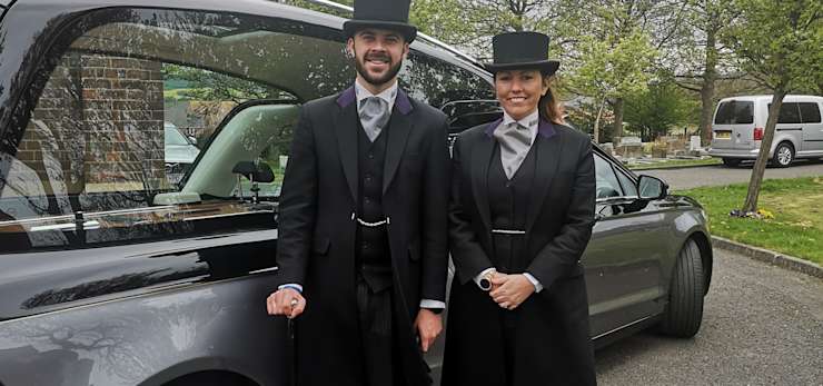 Husband and wife stood in front of a hearse.