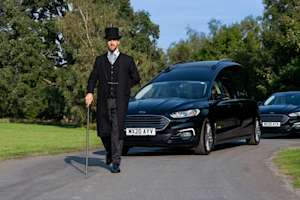Attendant leads a procession of vehicles down a road in parkland