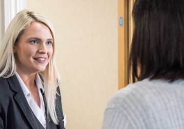 Blonde woman in a suit talking to a person with dark hair and a light top