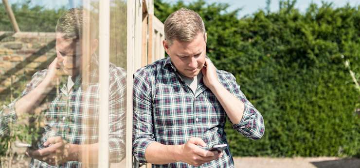 Guy texting on his phone in his garden.