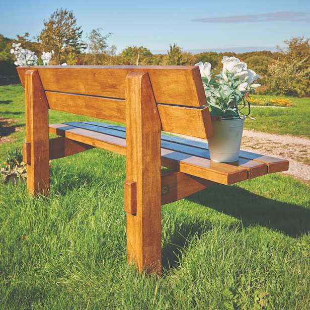 Wooden memorial bench on grass with a vase of white roses