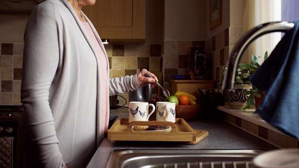 Lady making cups of tea in her kitchen.