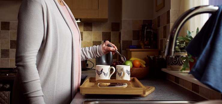 Lady making cups of tea in her kitchen.