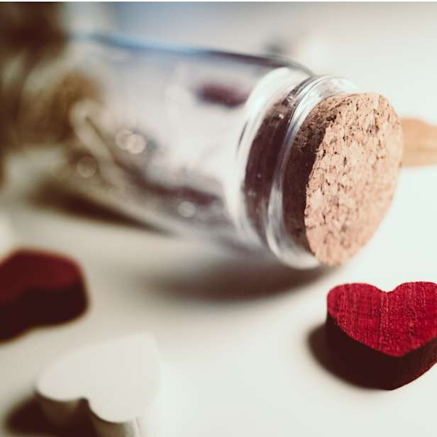 Glass corked jar on its side surrounded by red and white heart charms