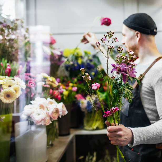 Person in a black hat and apron selecting flowers for a brightly coloured bouquet