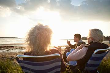 Family sat around in chairs on a beach watching the sunset.