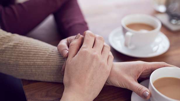 Family members holding hands providing support whilst having a cup of tea.