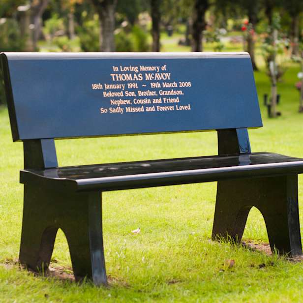 Black bench on grass with a gold inscription