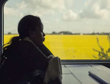 Woman in shadow looking out of window onto a yellow field