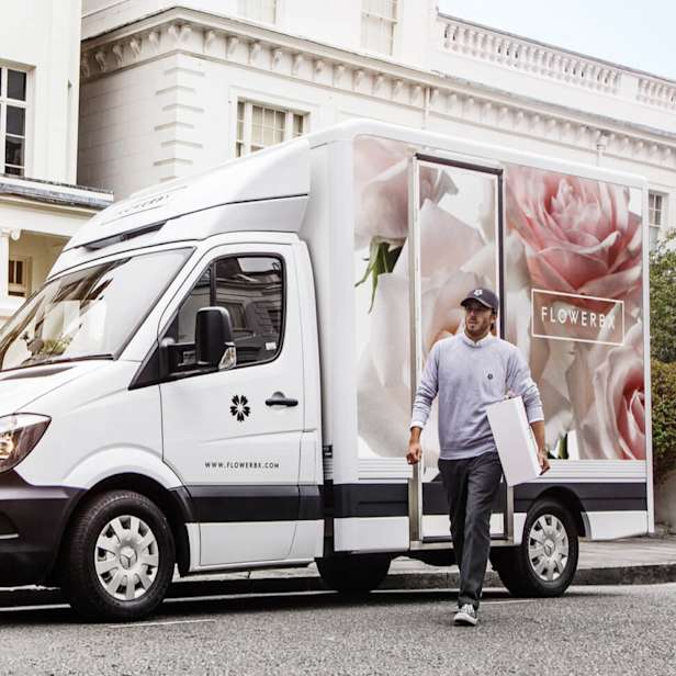 Person in front of a white van with flowers on carrying a box