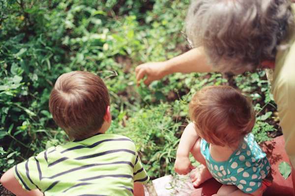 Two children look at a garden with a woman pointing