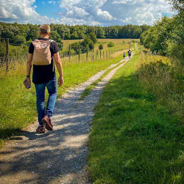 Short haired person with a canvas backpack walking down a country lane