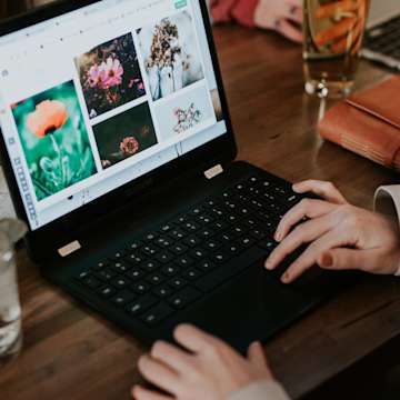 Hands at a laptop on a wooden desk with images of flowers on the screen