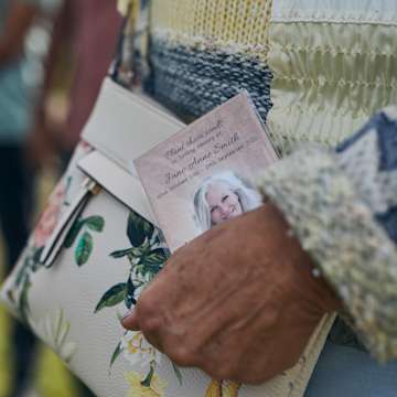 Hand holding a printed card against a cream handbag with flowers