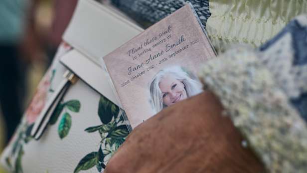 Hand holding a printed card against a cream handbag with flowers