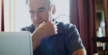 man holding his glasses, using his laptop