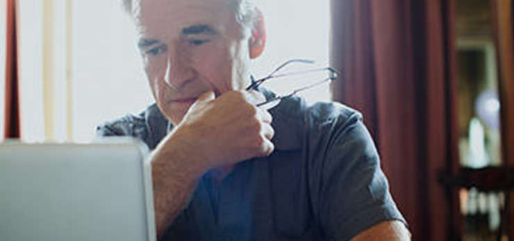 man holding his glasses, using his laptop