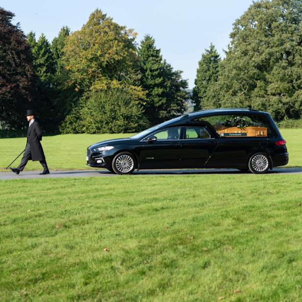 Black Hearse and attendant driving through parkland