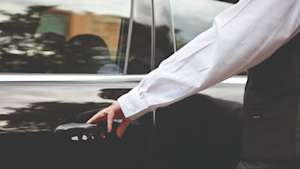 Black limousine door being opened by a funeral director.