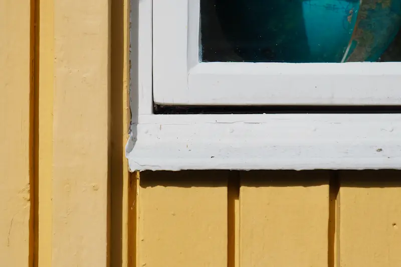 Trädgårdssidan har gulmålad träpanel och vitmålade fönsterlister.