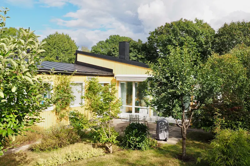 Trädgårdssidan har gulmålad träpanel och stora fönsterpartier.