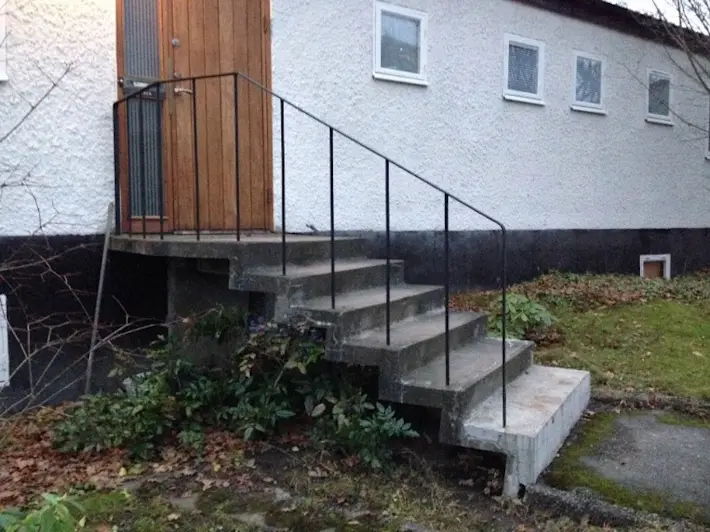 Ursprunglig gjuten betongtrappa med svartmålat smidesräcke.
