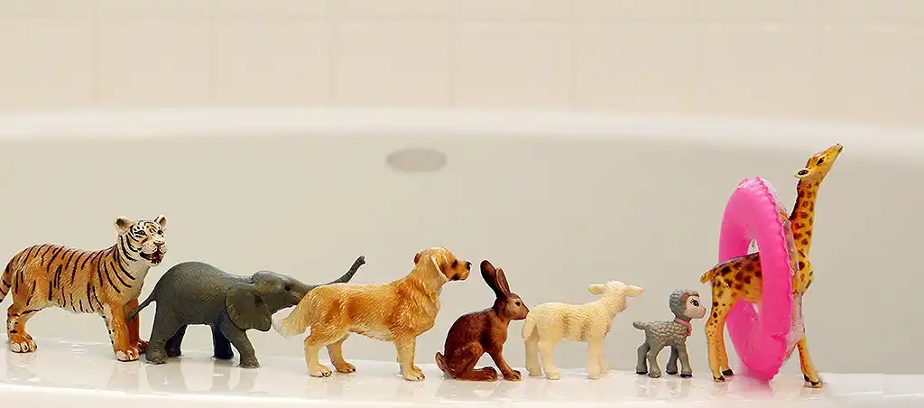 plastic animal toys lined up on the edge of a bathtub