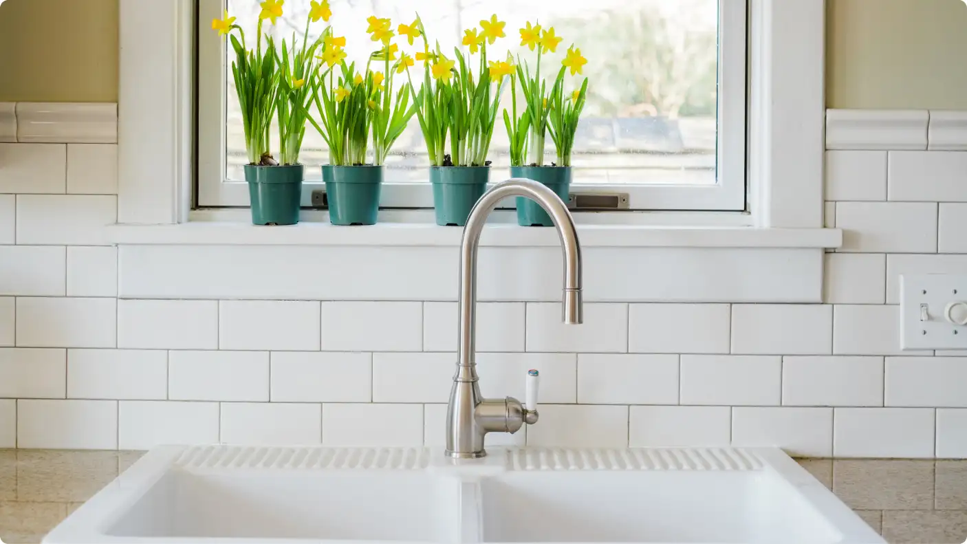 kitchen sink in front of white tile backsplash and window with daffodils