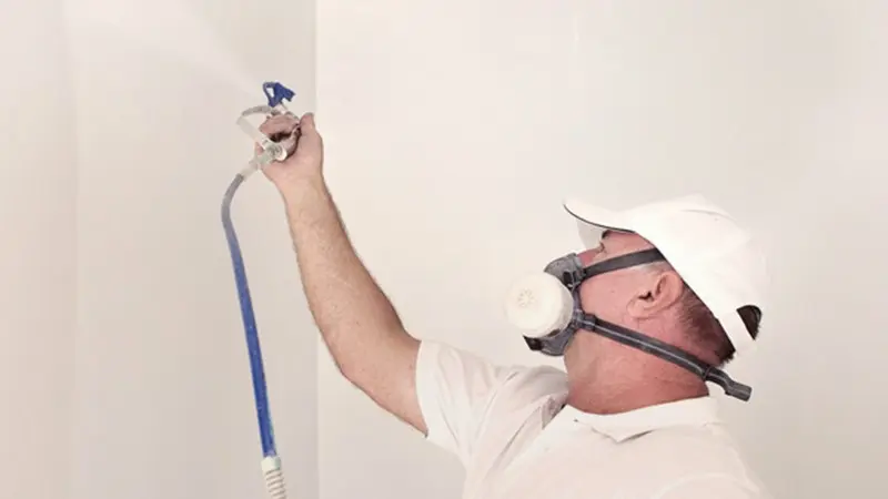 Painter spraying room with white paint