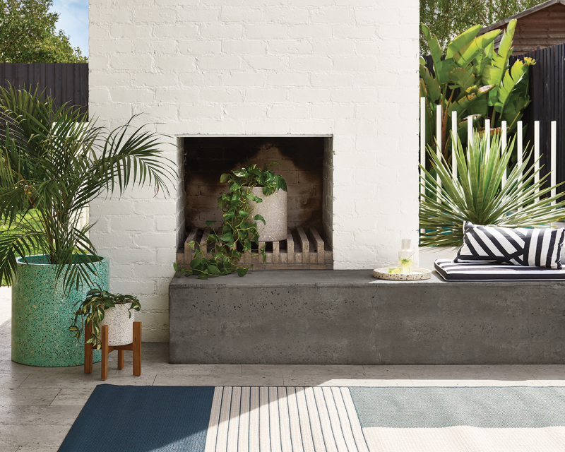 exterior outdoor fireplace: brick painted in beige surrounded by plants. 