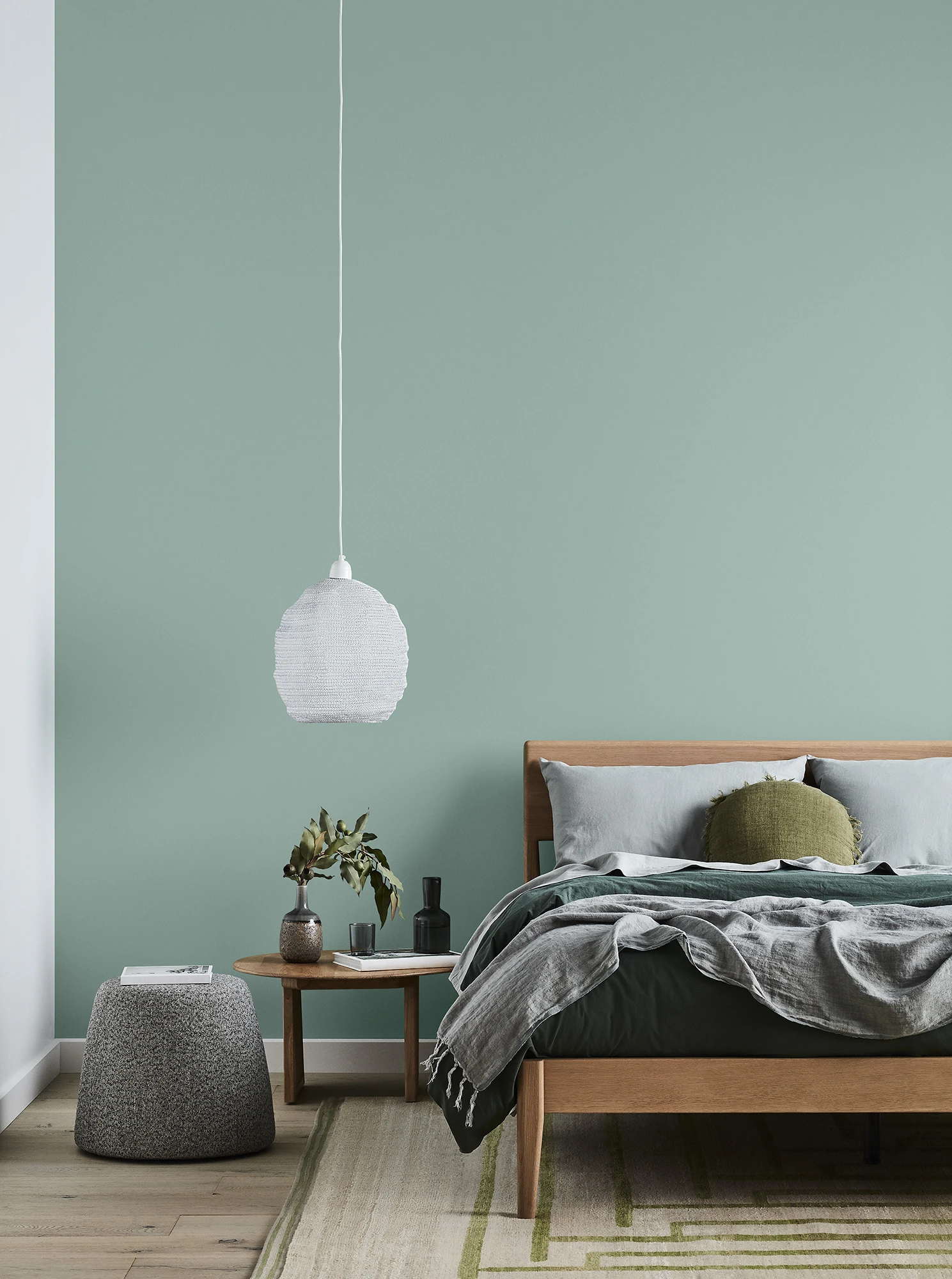 Green themed bedroom with bed, hanging lamp and bedside table to left.