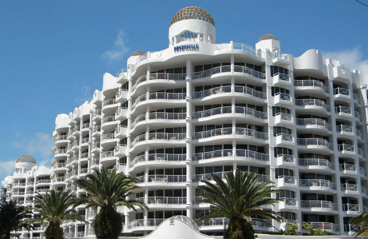 Exterior on multistorey white resort holiday apartments with palm trees in foreground.