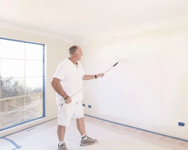 Male painter using roller to paint white interior wall.
