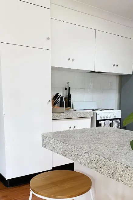 White kitchen with stove, speckled pattern benchtops and stool.