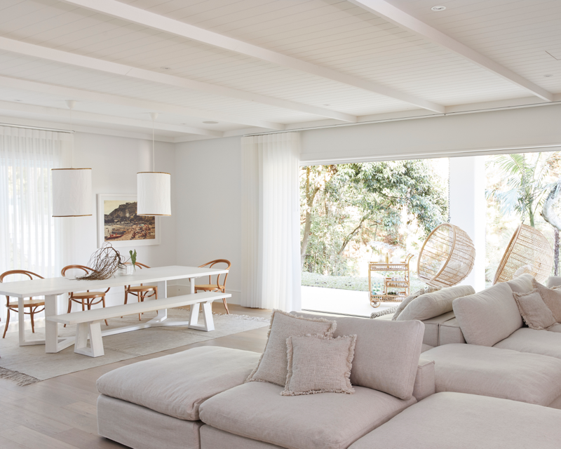 Hinterland Hideaway's living and dining spaces in Dulux White on White open out to verandah with two hanging cane seats