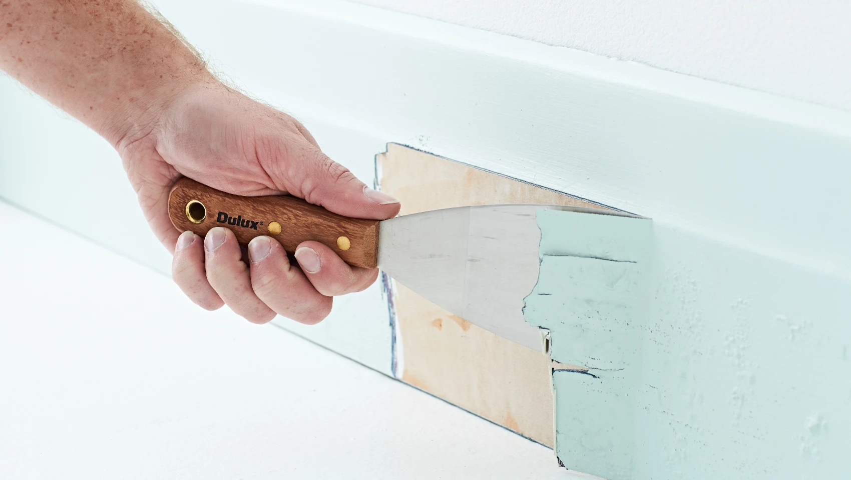 Man removing paint from skirting board with paint scraper.