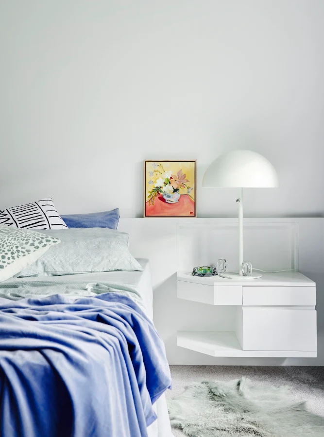 Bedroom wall painted in Dulux Ōkārito white with colourful artwork, modern lamp and blue bedding.