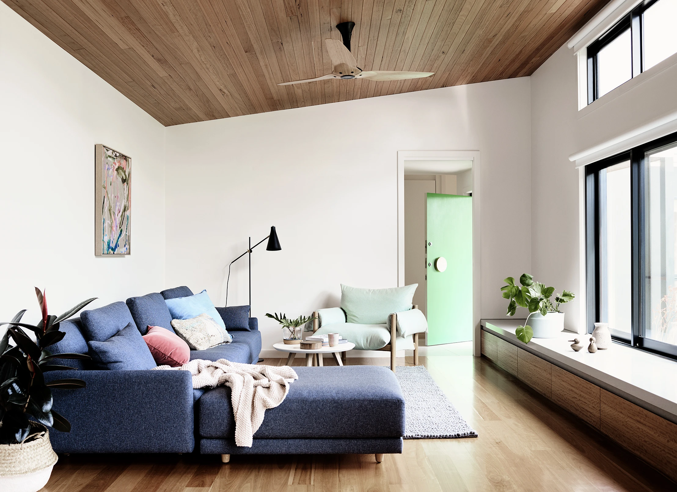 White living room with timber ceiling, blue couch and bright green door.