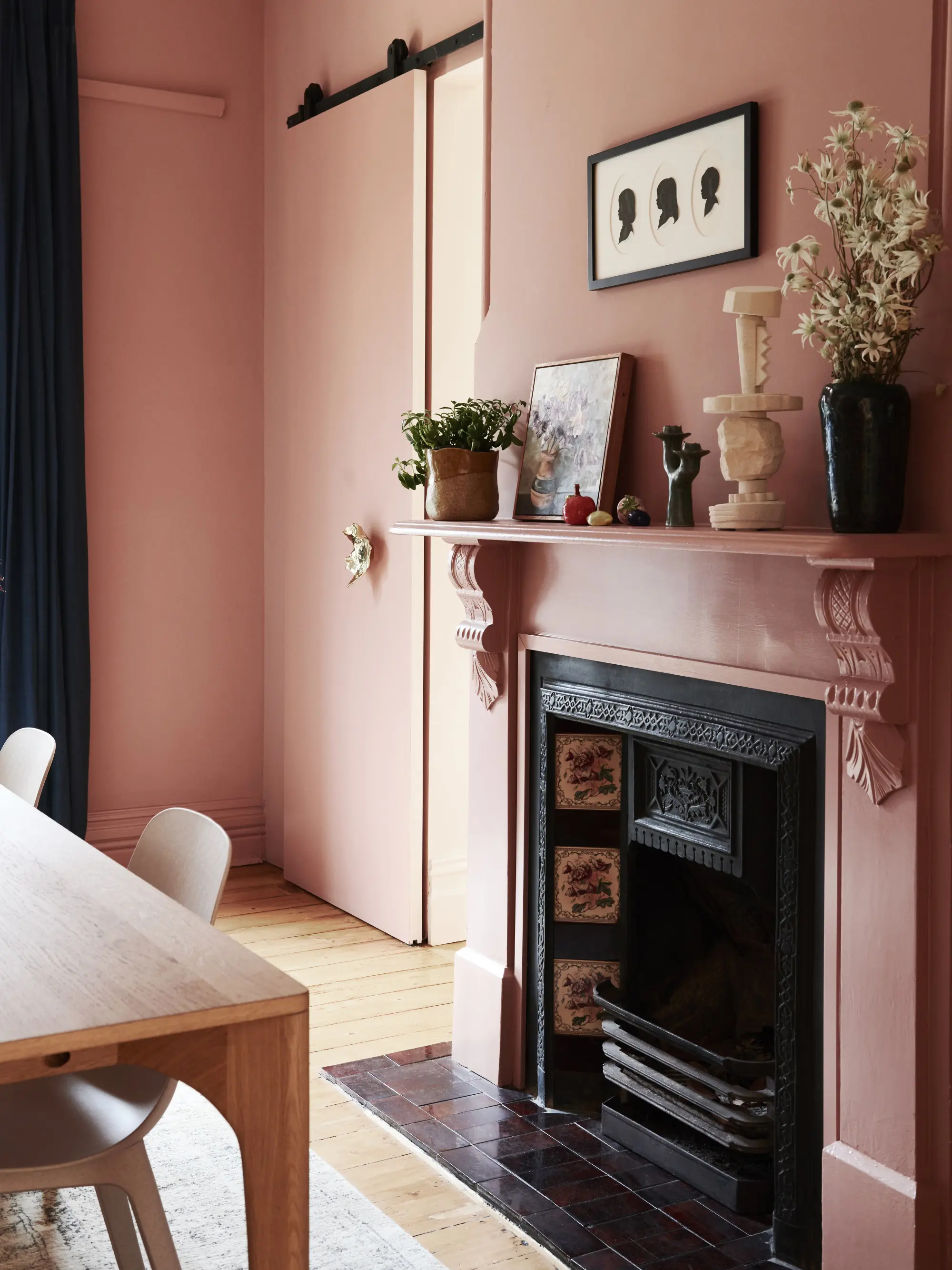 A dining room with fireplace. The walls and fireplace surrounding are all painted a dusky pink colour