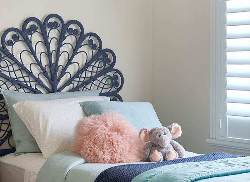 A bedhead on a bed with a fluffy pink cushion and an elephant soft toy