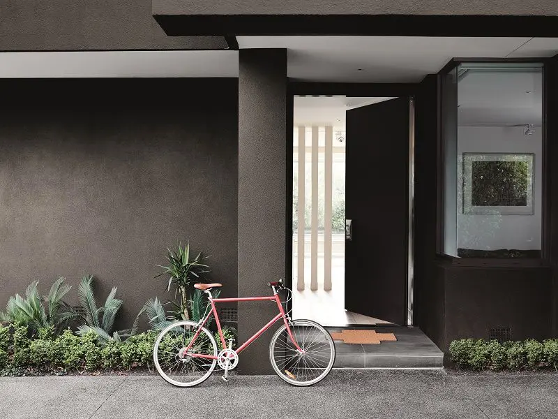 Bicycle leaning against exterior of modern dark grey house.
