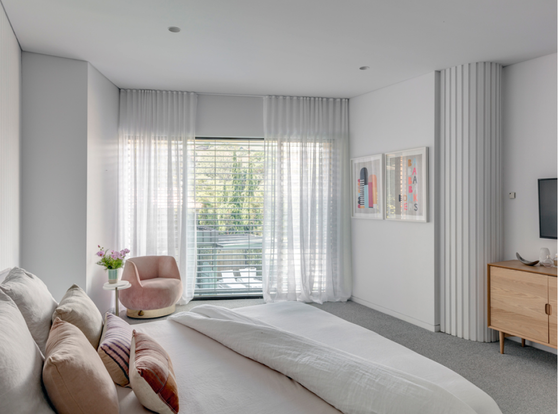 interior white bedroom with pink chair and windows.