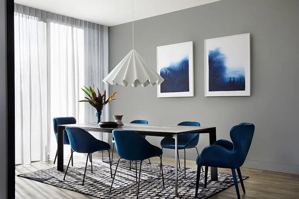 Interior grey dining room with blue chairs and painting. 