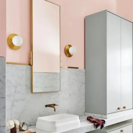 Bathroom featuring mirror and sink with a feature wall using grey slate on the bottom half and pink paint on the top half with gold tap wear.