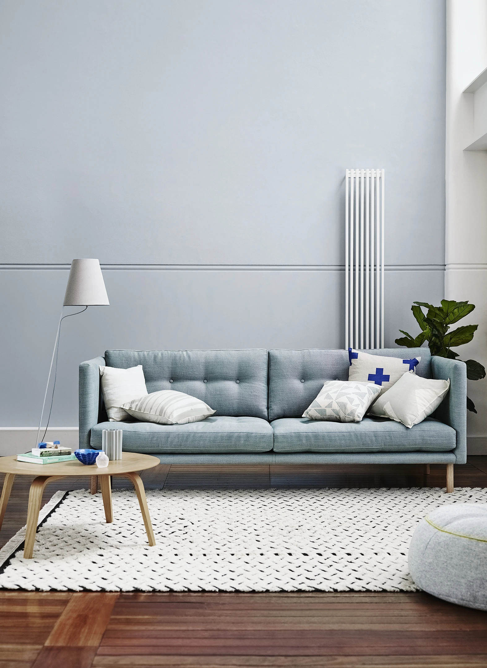 Blue couch in wooden floors with white rug in front of it and floor lamp