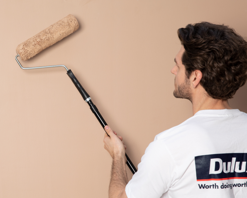 Painter rolling neutral coloured paint on a wall with a roller - Dulux Professional® range