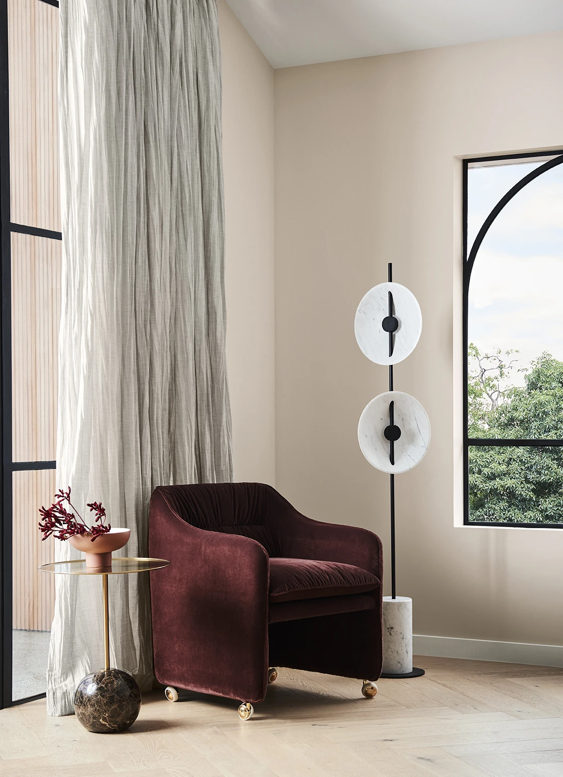 Corner with red velvet chair against wall, sheer curtains on window and lamp next to chair. 