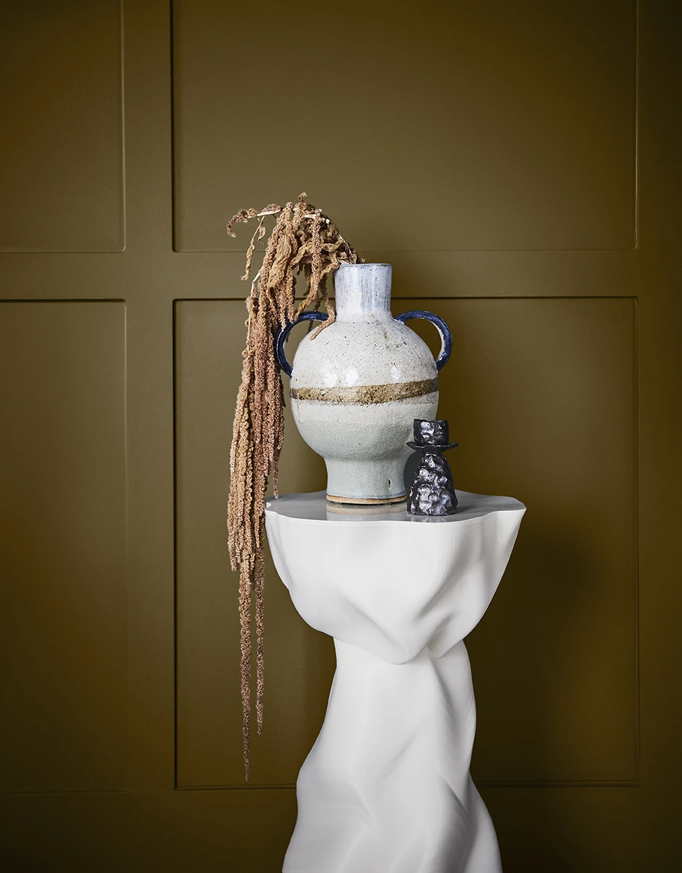 Ceramic vase on white pedestal against khaki wall